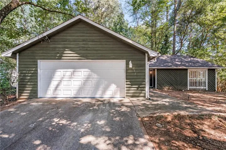 Green horizontal siding, attached garage with panel door, asphalt shingle roof, concrete driveway, and front entry