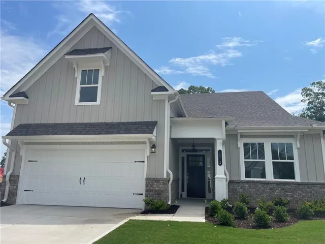 Contemporary home exterior featuring board and batten siding, dark shingle roofing, and a brick accent foundation
