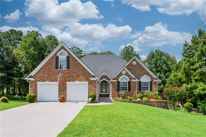 Brick Colonial home featuring a two-car garage with white panel doors, arched entryway with sidelights, multiple multi-pane windows, and a manicured lawn bordered by mature landscaping and brick hardscaping