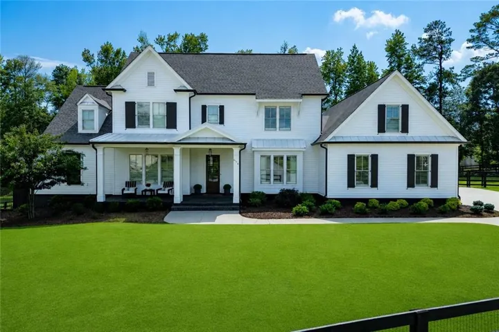 White siding exterior with black shutters, dark shingle roof, covered front porch, and paved driveway
