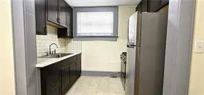 Kitchen with freestanding refrigerator, light countertops, decorative backsplash, and dark cabinetry