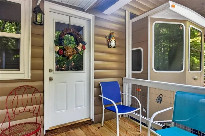 Exterior featuring wood-look siding, a paneled door with an integrated window, a wall-mounted exterior light fixture, and a wood-finish porch floor