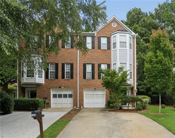 Brick exterior with bay windows, black shutters, white garage doors, and mature landscaping