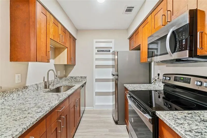 Kitchen with appliances with stainless steel finishes, light stone counters, and brown cabinets Kitchen with appliances with stainless steel finishes, light stone counters, and brown cabinets