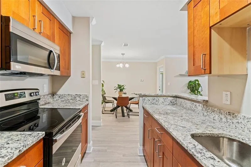 Kitchen with stainless steel appliances, ornamental molding, light stone countertops, light wood-type flooring, and a chandelier Kitchen with stainless steel appliances, ornamental molding, light stone countertops, light wood-type flooring, and a chandelier
