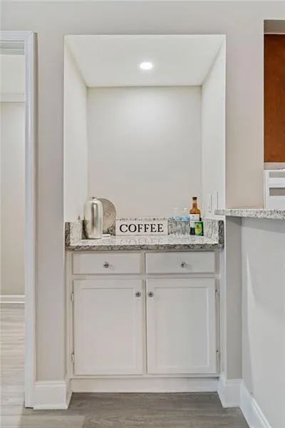 Bar featuring white cabinets, light stone counters, and light wood-type flooring Bar featuring white cabinets, light stone counters, and light wood-type flooring