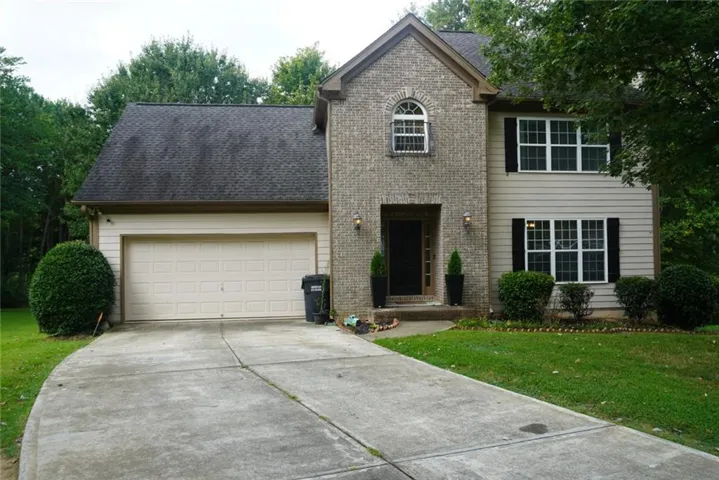 Brick and siding exterior with a gabled roofline, featuring a two-car garage, arched window, and landscaped shrubbery