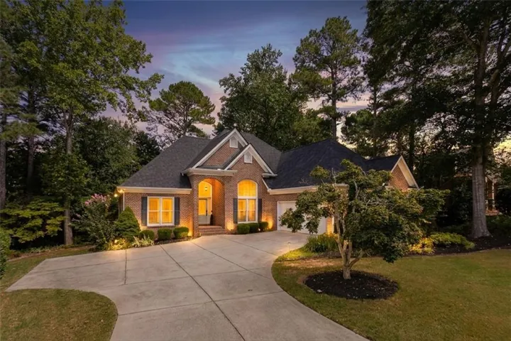 Brick exterior with dark shutters, arched entry, concrete driveway, and mature landscaping