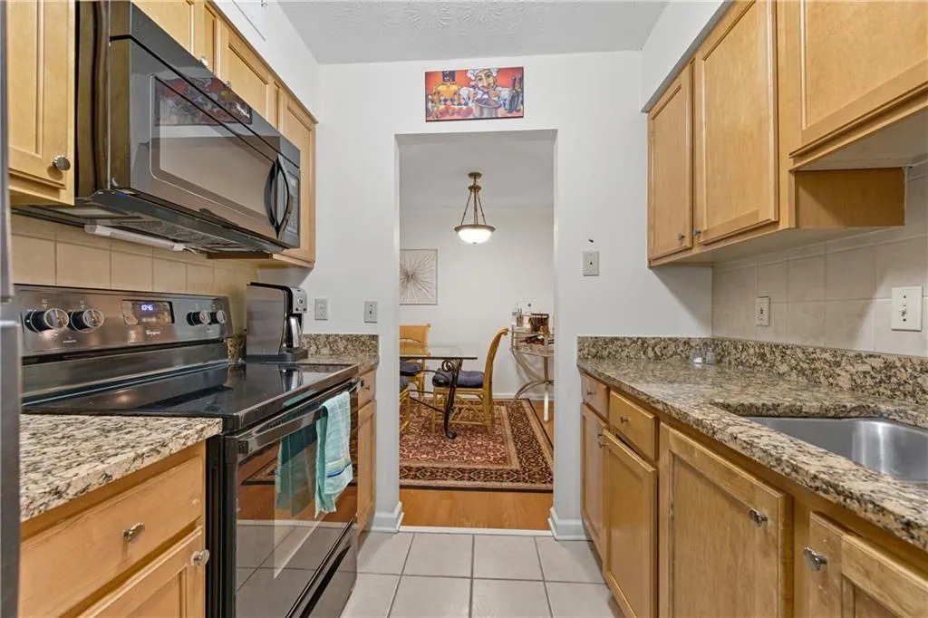 Kitchen featuring tasteful backsplash, black appliances, light stone counters, and light tile patterned floors