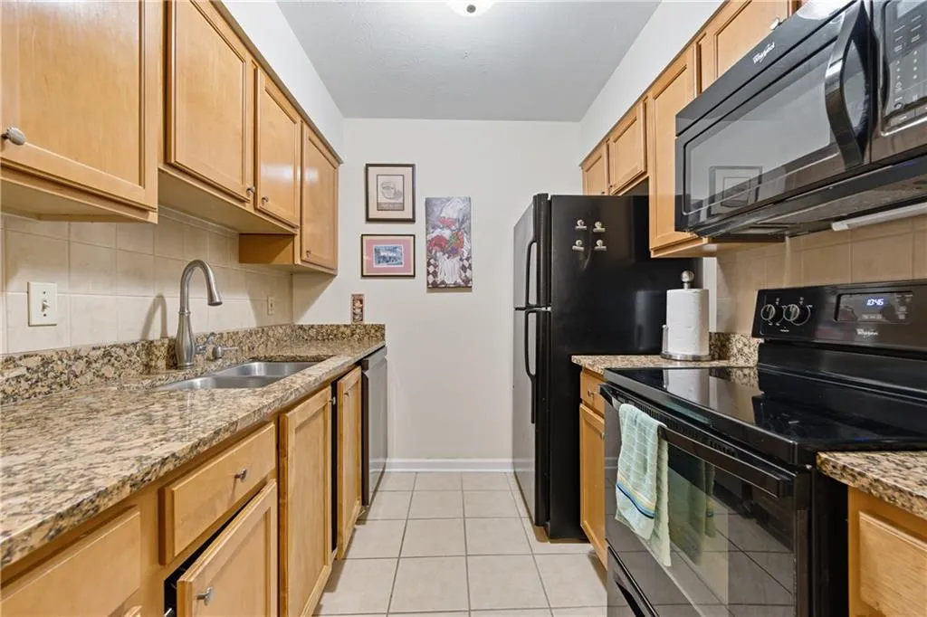 Kitchen with tasteful backsplash, black appliances, light stone counters, and light tile patterned floors