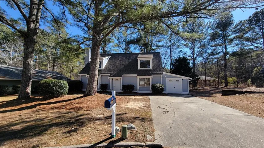 View of front of home with driveway, view of wooded area, and stucco siding