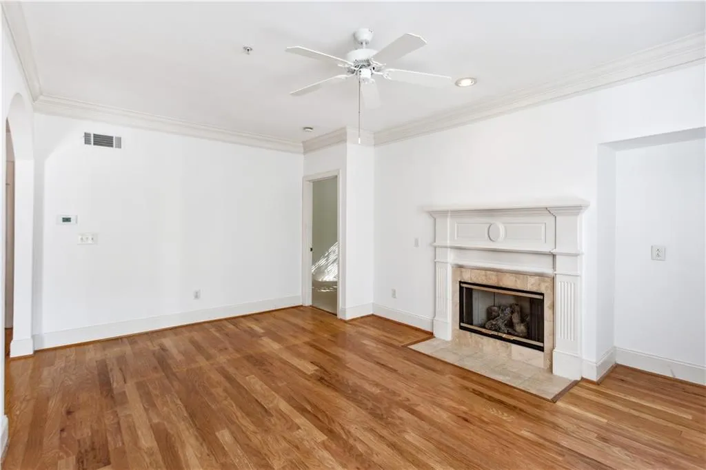 Unfurnished living room with a tile fireplace, crown molding, light wood-type flooring, and ceiling fan