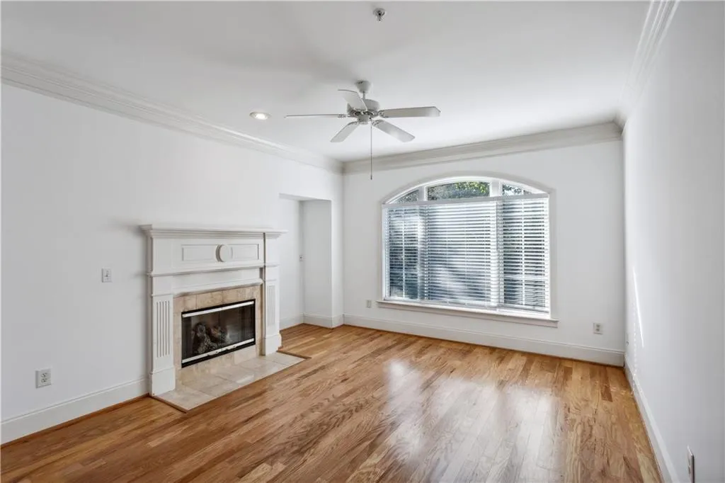 Unfurnished living room with crown molding, a tiled fireplace, light wood-type flooring, and ceiling fan