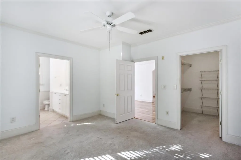Unfurnished bedroom featuring ceiling fan, a spacious closet, crown molding, a closet, and light colored carpet