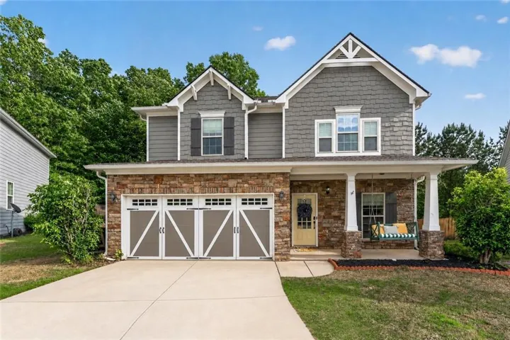Two-story residence featuring a stone and shingle facade, a covered front porch with white columns, and a double-wide driveway