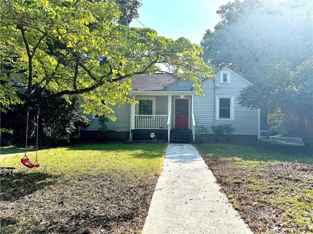 Exterior featuring light gray siding, a red front door, a covered porch with white railings, a concrete walkway, and mature trees