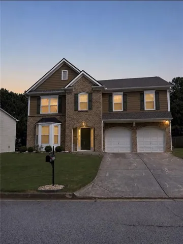 Two-story residence featuring a brick and siding exterior, bay window, two-car garage, and established front lawn