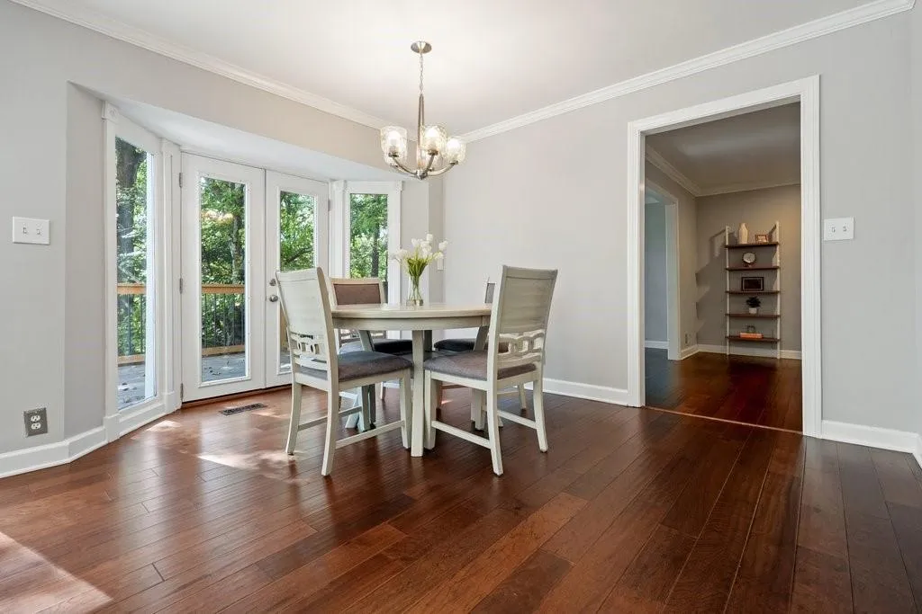 Dining area featuring wood-finish flooring, crown molding, a multi-bulb chandelier, and French doors