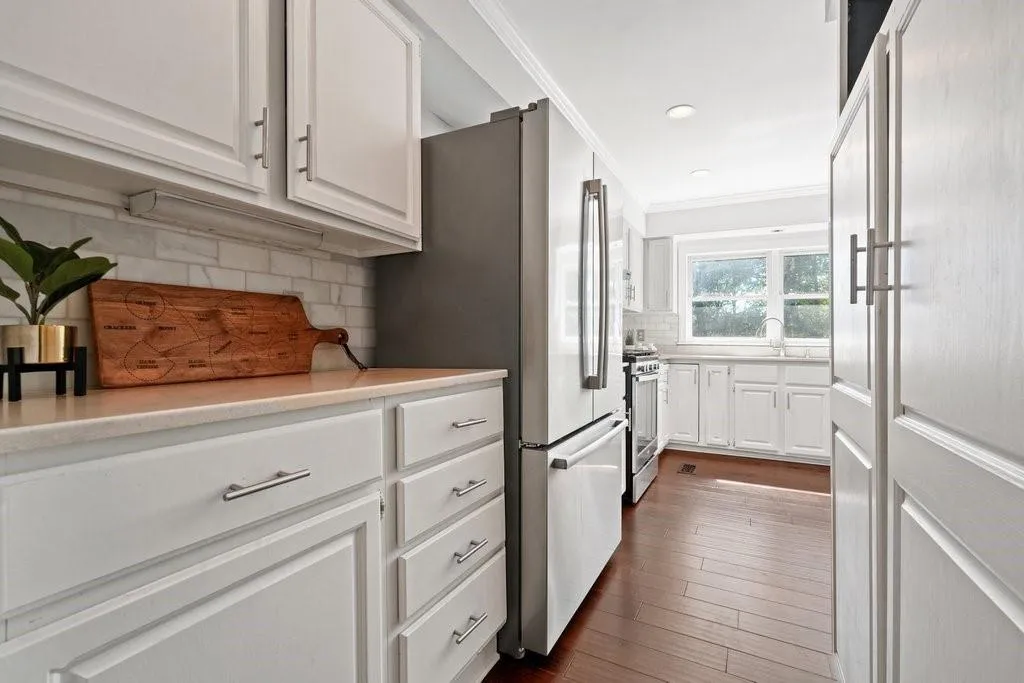 Kitchen featuring white shaker-style cabinetry, stainless steel appliances, subway tile backsplash, and wood-finish flooring