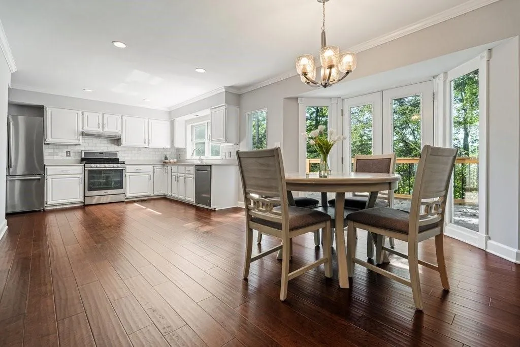 Kitchen featuring white cabinetry, wood-finish flooring, stainless steel appliances, a multi-light chandelier, and bay windows with access to an exterior deck