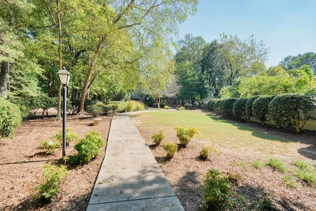 Concrete walkway bordered by manicured lawn, structured hedging, mature trees, and pedestal landscape lighting