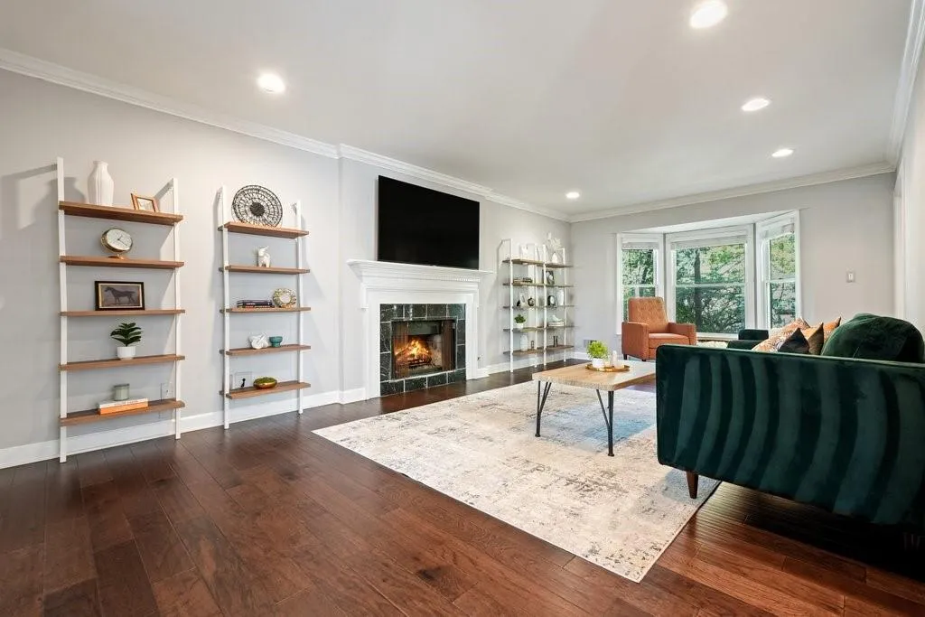 Living area featuring wood-finish flooring, recessed lighting, crown molding, a bay window, and a fireplace with stone tile surround and white mantel