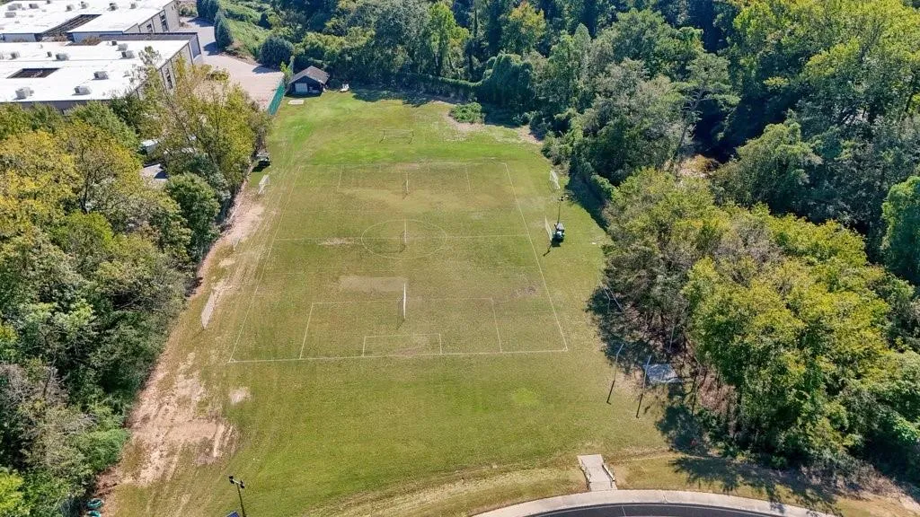 Expansive level lot featuring a marked grass athletic field, perimeter mature trees, and a small utility structure