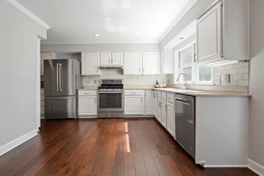 Kitchen featuring white shaker-style cabinetry, stainless steel appliances, subway tile backsplash, solid-surface countertops, and wood-finish flooring