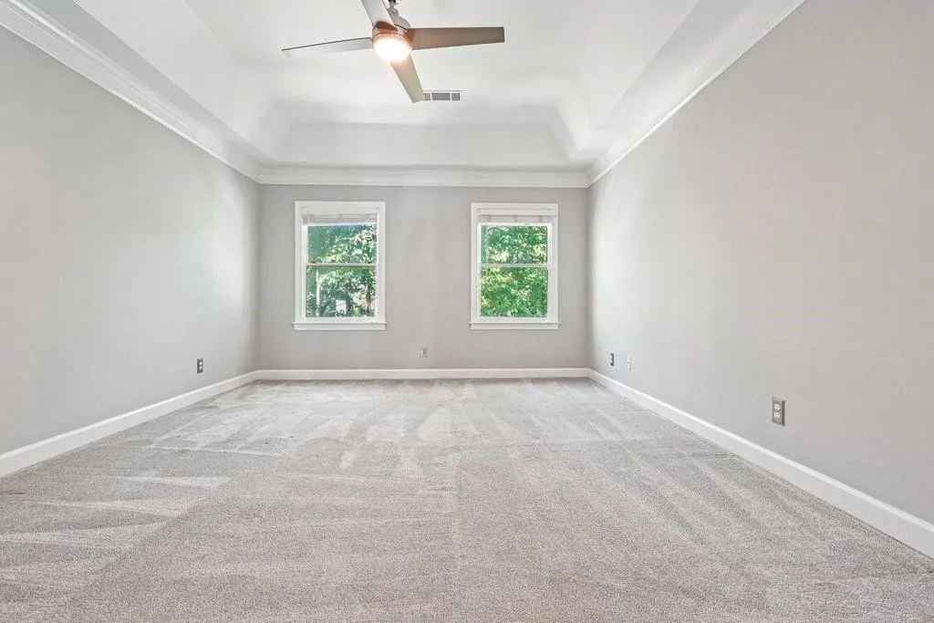Tray ceiling, neutral wall tones, plush wall-to-wall carpeting, dual windows, and an integrated ceiling fan with light fixture
