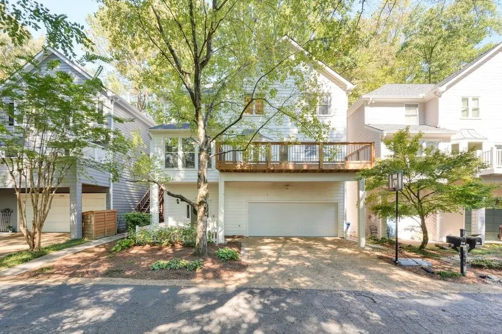 Two-story residence featuring horizontal siding, a raised deck with metal railings, a double-car garage, and mature landscaping
