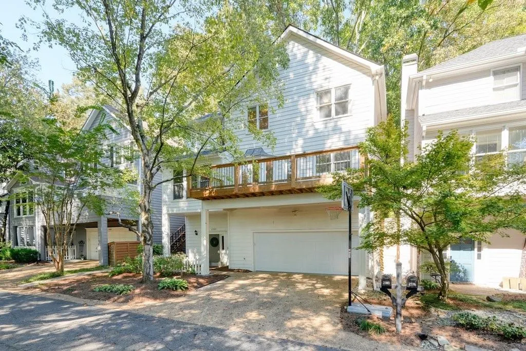Two-story residential exterior featuring horizontal siding, a second-level wooden balcony with railing, and an attached two-car garage