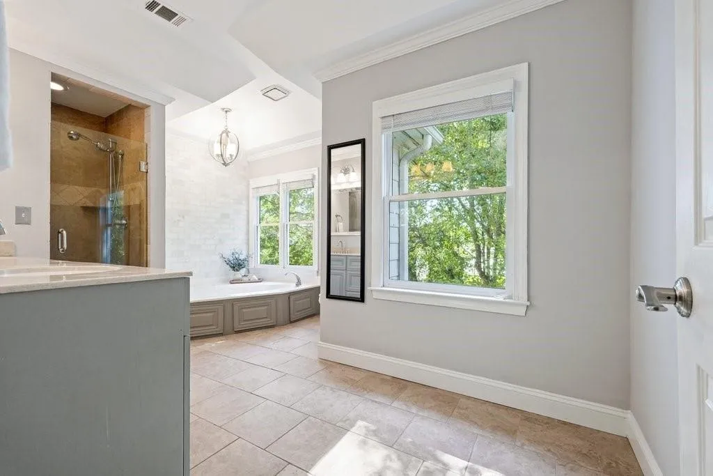 Bathroom featuring neutral ceramic tile flooring, a built-in corner soaking tub with a tiled surround, a glass-enclosed shower with tiled walls, crown molding, and double-hung windows