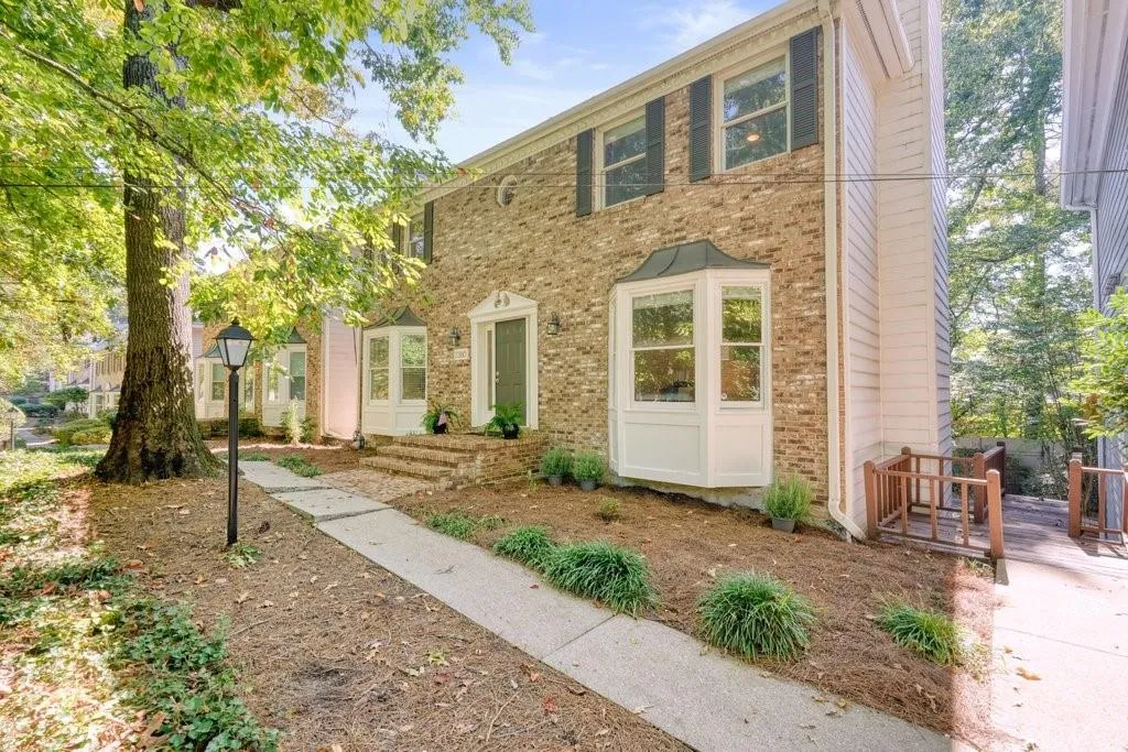 Two-story brick exterior featuring multiple bay windows, decorative shutters, a covered entry with brick steps, and an attached wood staircase