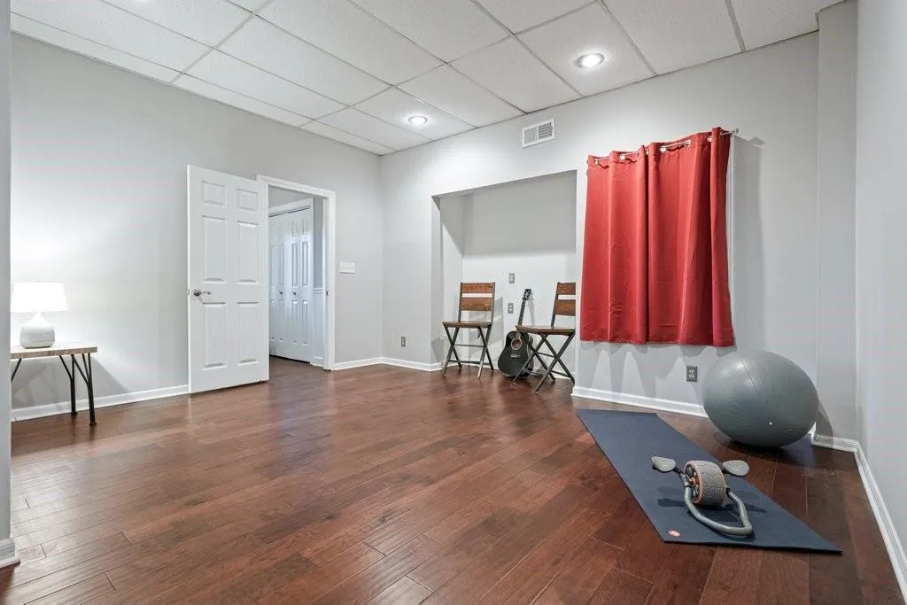 Interior space featuring wood-finish flooring, a recessed alcove, drop ceiling with integrated lighting, and a six-panel interior door