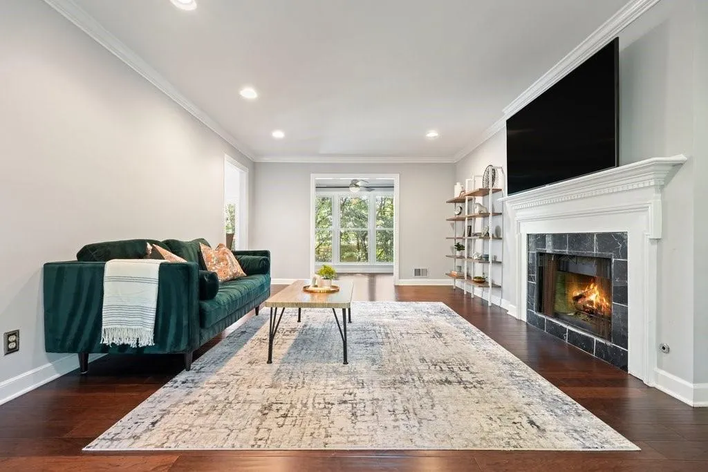 Living area featuring dark wood-finish flooring, recessed lighting, crown molding, and a fireplace with a stone-style surround and decorative white mantle