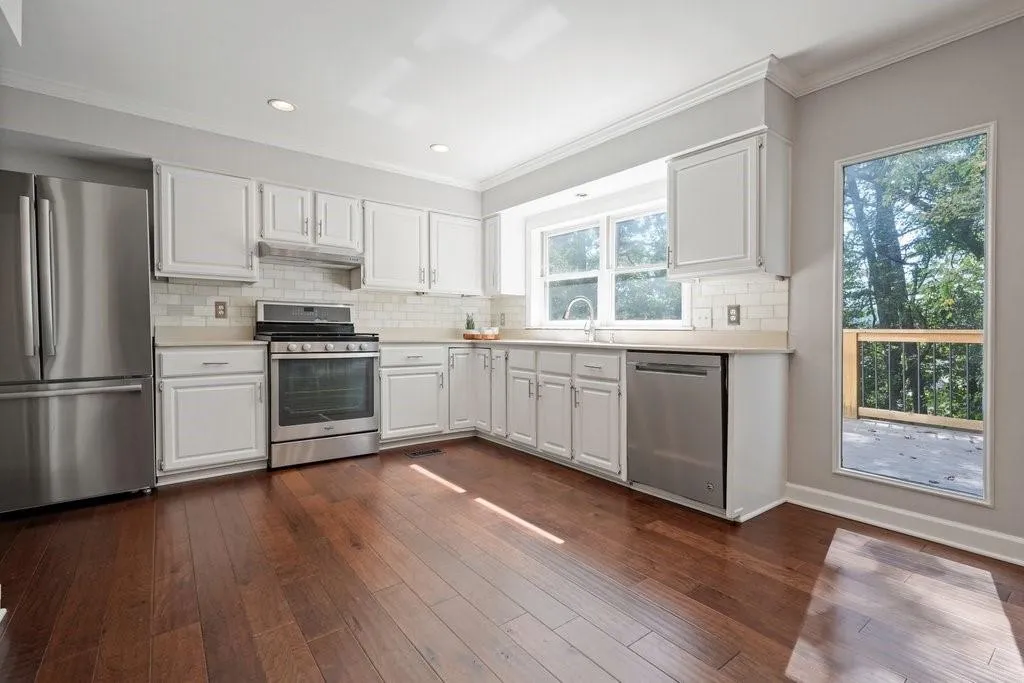 Kitchen featuring white cabinetry, stainless steel appliances, subway tile backsplash, wood-finish flooring, and a window providing natural light