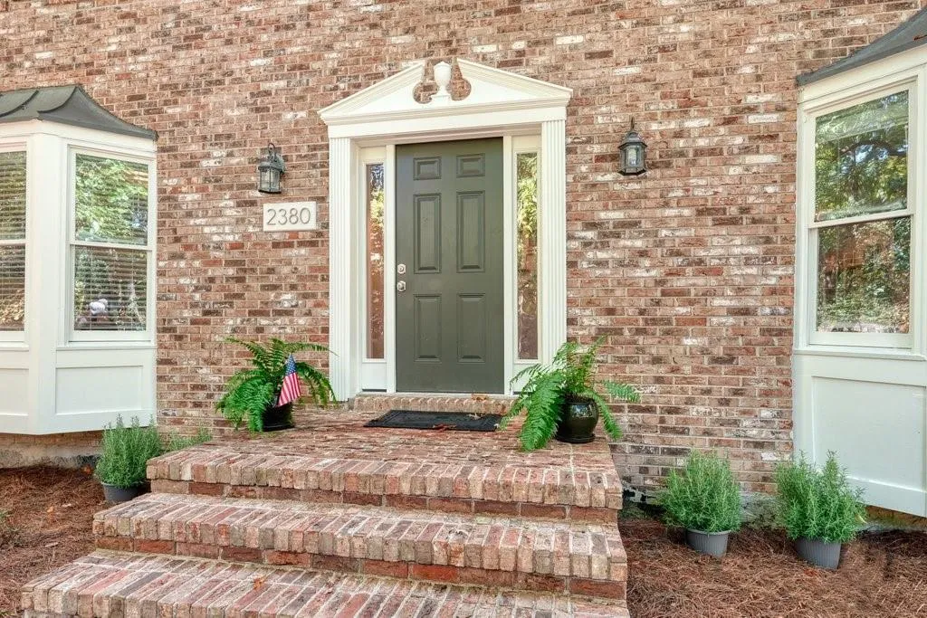 Multi-toned brick exterior featuring symmetrical bay windows, a column-framed entryway with decorative pediment, and tiered masonry steps