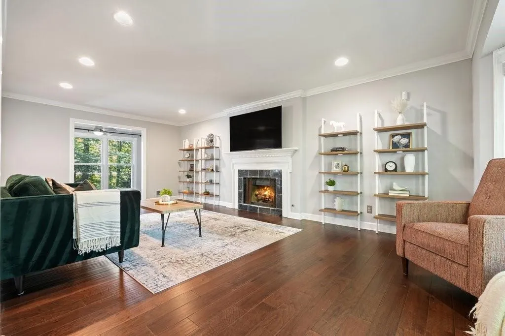 Living area featuring wood-finish flooring, recessed lighting, crown molding, and a fireplace with a decorative mantel and tile surround