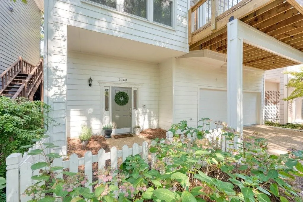 Two-story exterior featuring white horizontal siding, a covered entryway with a solid-paneled door and sidelights, a raised wood deck, and a multi-car garage with white doors