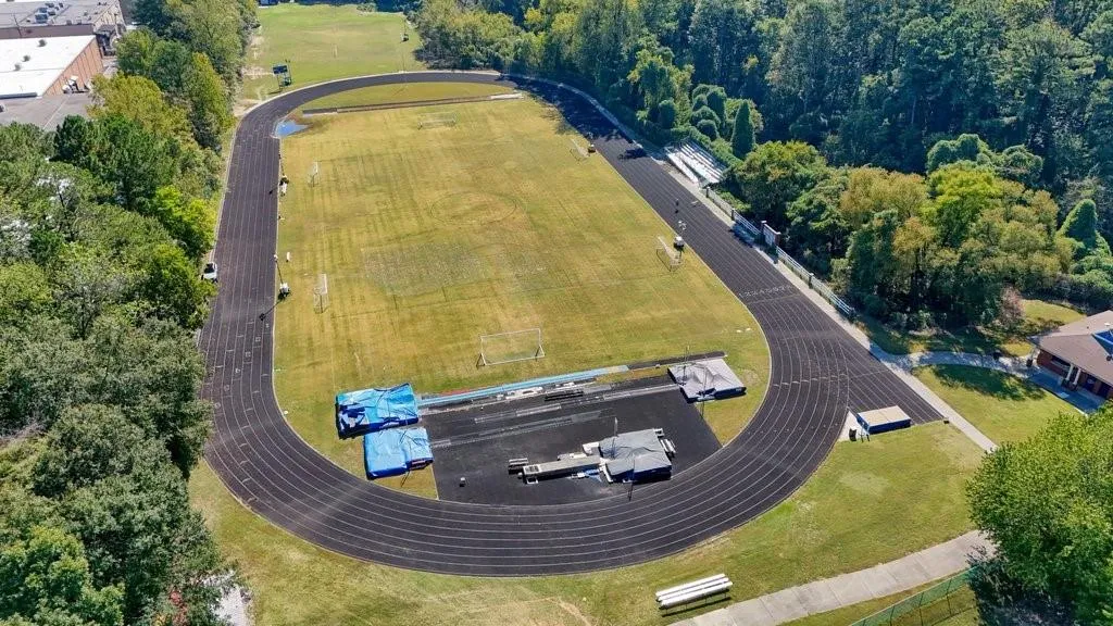 Multi-lane asphalt running track encompassing a central turf field, integrated bleacher seating, and surrounding mature landscaping