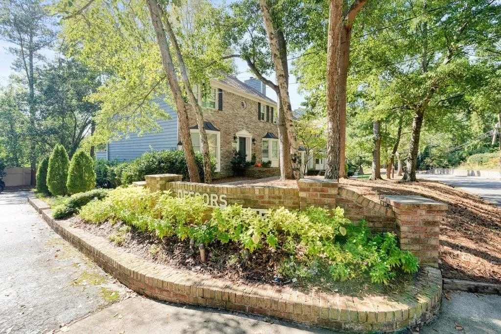 Exterior featuring a brick and stone monument sign, masonry retaining wall, mature deciduous trees, and a two-story residence with a stone facade and shingle siding