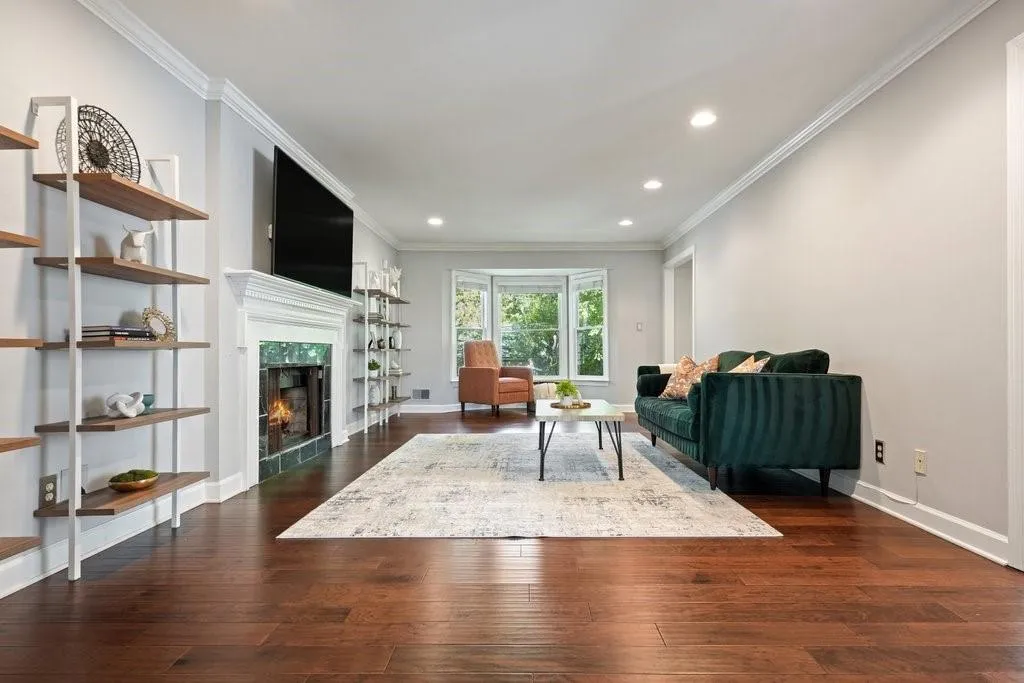 Living area featuring wood-finish flooring, a fireplace with a decorative mantel, crown molding, recessed lighting, and a bay window