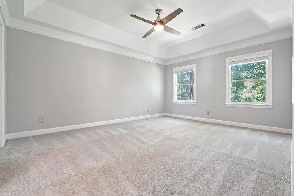 Tray ceiling featuring crown molding, neutral wall color, wall-to-wall carpeting, dual windows, and a central ceiling fan