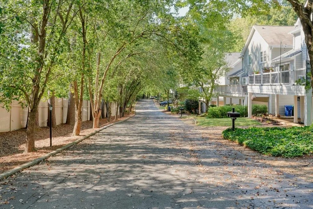 Asphalt driveway bordered by mature trees, privacy fencing, and elevated rear deck with metal railing