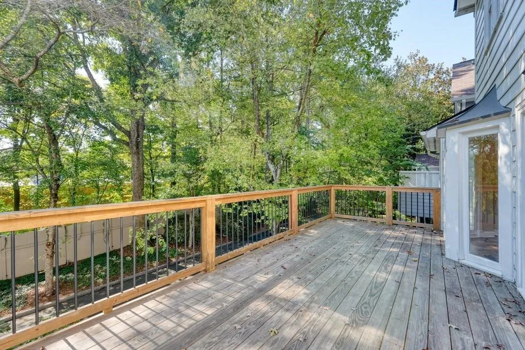 Elevated wooden deck featuring metal balusters, wooden handrails, and mature tree-lined surroundings