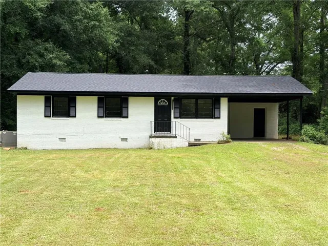 White brick exterior with black shutters, black front door, and a covered carport