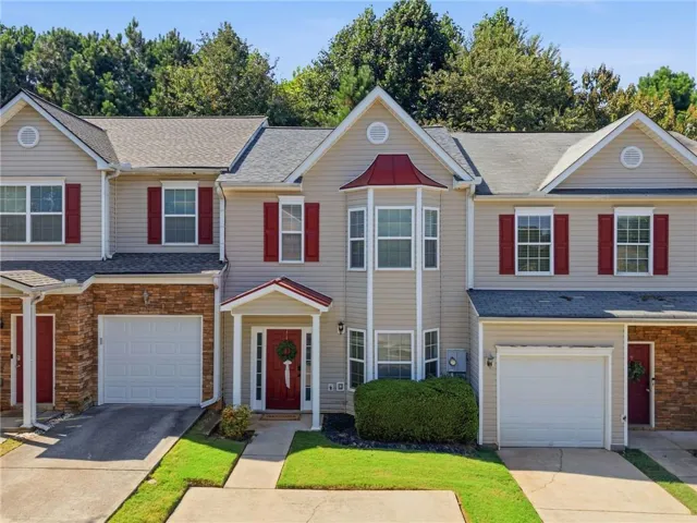 Two-story townhome with light-colored siding, red shutters, and stone veneer accents