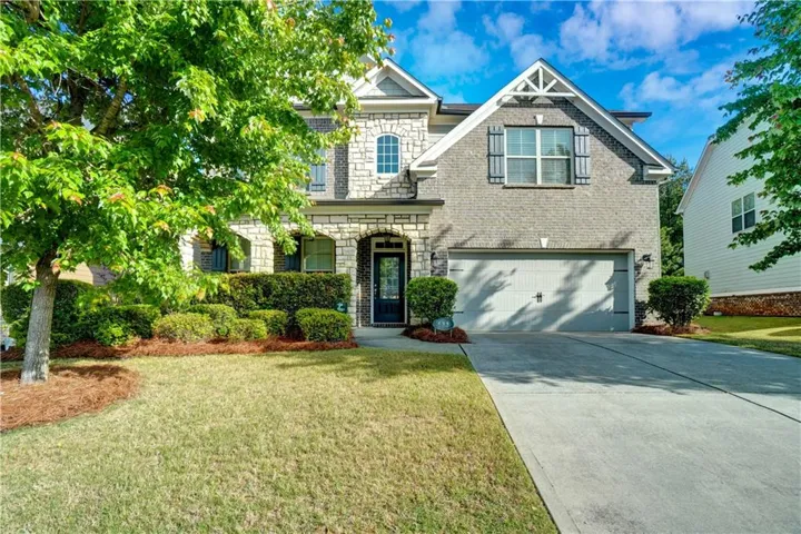 Two-story residence featuring a gray brick and stone veneer facade, a two-car garage, and a concrete driveway