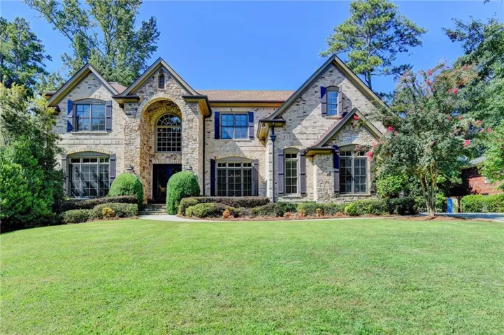 Stone facade with multiple gables, arched entry, and a symmetrical front lawn