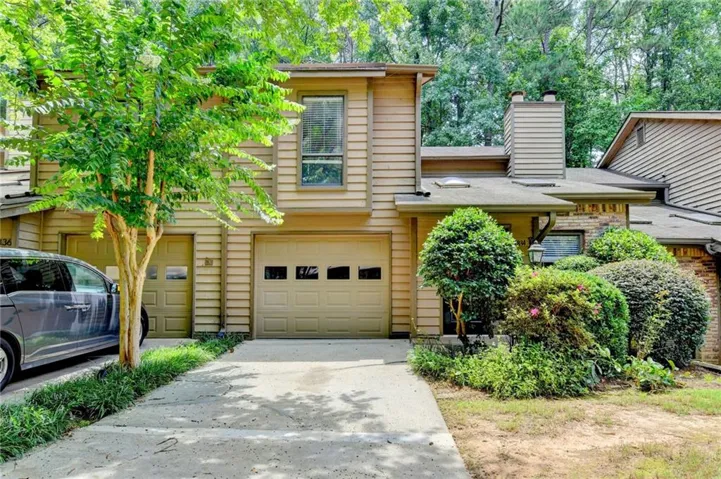 Exterior featuring two single-car garages, wood siding, and mature landscaping